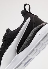 Black and white athletic shoe made of mesh and synthetic materials, featuring a textured sole, prominent branding, and a pull tab at the heel.