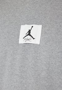 Tissu gris avec un patch carré blanc montrant une silhouette noire d'un joueur de basket sautant avec un ballon et le mot « Flight » en dessous.
