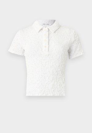 Bijela teksturirana polo majica kratkih rukava s ovratnikom i četiri gumba sprijeda.