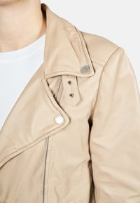 Béžová kožená moto bunda se zipem, velkým límcem a stříbrnými detaily. Měkká struktura a přiléhavý střih.