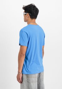 Gaiši zils T-krekls, kas izgatavots no mīksta, viegla materiāla. Tam ir apaļa kakla izgriezne un īsas piedurknes, kā arī neliels logo uz piedurknes.