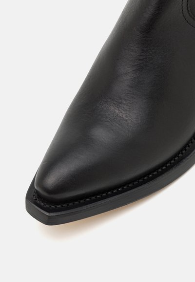 Botine negre din piele, cu vârf ascuțit, margine curbată și detalii cusute de-a lungul tălpii, având o textură netedă și lustruită.