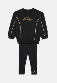 Tricou de trening negru cu accente albe, logo auriu "Jordan" pe piept, asortat cu colanți negri cu un mic logo auriu la gleznă.
