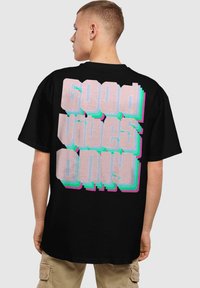 Sort t-shirt med stort retro-stil tekst på ryggen i pink og blå, der står "Good Vibes Only." Korte ærmer, normal pasform.