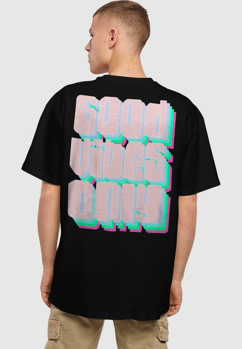 Sort t-shirt med stort retro-stil tekst på ryggen i pink og blå, der står "Good Vibes Only." Korte ærmer, normal pasform.