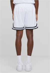 Shorts de sport blancs avec des rayures noires sur les côtés, taille élastique et texture lisse, associés à des baskets blanches et des chaussettes mi-mollet.