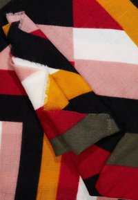 Écharpe en mélange de laine présentant des motifs géométriques en rouge, rose, blanc, jaune, noir et vert. Les bords sont effilochés pour ajouter de la texture.