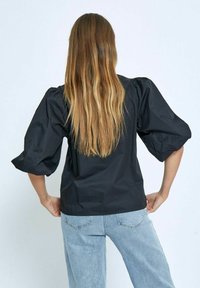 Camicia nera con maniche a palloncino, caratterizzata da una texture liscia e una vita aderente, abbinata a jeans in denim azzurro chiaro, vista da dietro.