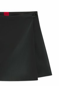 Black skirt made of smooth material with a pleated design. Features a button closure and a red label at the waistband.