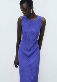 Fitted sleeveless dress in vibrant blue with black polka dots. Made of smooth fabric, features a round neckline and a minimalistic design.