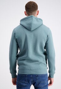 Debeszila kapuciņa izgatavota no mīkstas auduma, tai ir kenguru kabata, ribotas piedurknes un apakšmala, kā arī aukliņa kapucē un gluda tekstūra.