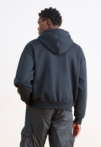 Sudadera negra con capucha de ajuste holgado, puños y dobladillo acanalados, y textura suave. Se lleva con pantalones cargo negros con bolsillos laterales.