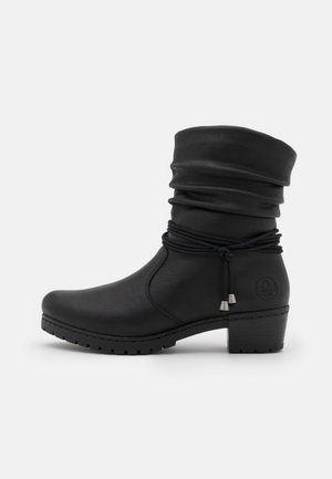 Black ankle boot with a slouchy shaft, made of leather-like material, featuring a textured surface, decorative knot, and a chunky heel.