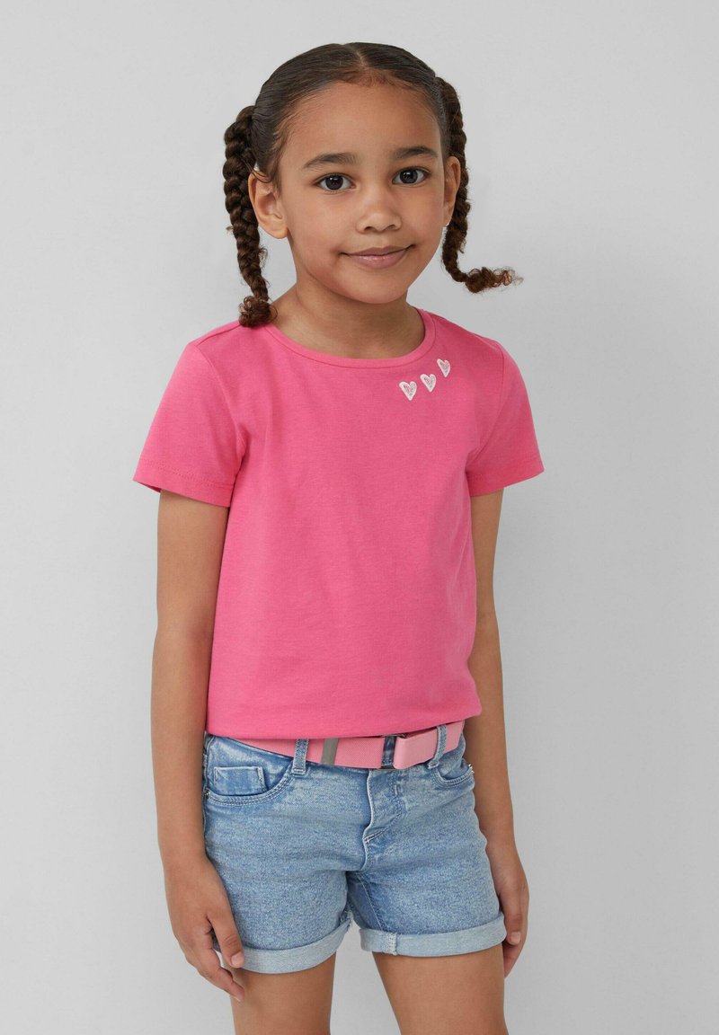 Roze T-shirt met korte mouwen met drie kleine hartontwerpen bij de halslijn, gecombineerd met lichtblauwe denim short en een roze riem.