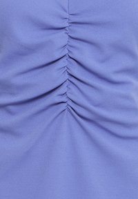 Tissu violet clair avec des fronces rassemblées au centre, créant des plis verticaux et de la texture.