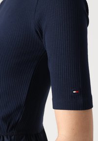 Námořnický pruhovaný top s krátkými rukávy, který má na rukávu malé logo v červené, bílé a modré barvě, a fitted střih v pase.