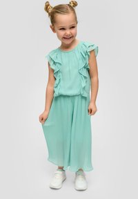 Mintgroen twee-delige outfit met ruches aan de mouwen en geplooide broek. Lichtgewicht stof met een zachte textuur. Draagt met witte sneakers.