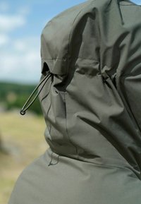 Jachetă verde impermeabilă cu glugă. Materialul este neted, cu șnururi elastice pentru ajustare. Design minimalist, fără broderii.