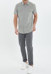 Camisa de botones de manga corta de color gris claro con dos bolsillos en el pecho, combinada con pantalones grises y zapatillas blancas. Diseño y corte simples y limpios.