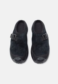 Musta liukupohjallinen kengät, jotka on valmistettu mokasta ja joissa on kumiyksityiskohtia. Ominaisuuksiin kuuluu hihnakiinnitys, teksturoitu sisäpohja ja kaareva ulkopohja, joka tarjoaa pitoa.