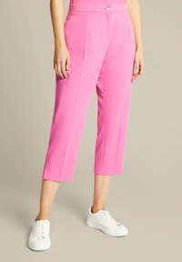Roze cropped broek met een gladde textuur, voorzien van een knoopsluiting en zijzakken, gecombineerd met witte sneakers.
