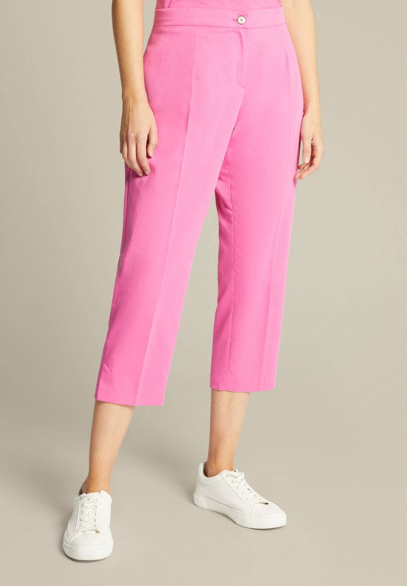 Roze cropped broek met een gladde textuur, voorzien van een knoopsluiting en zijzakken, gecombineerd met witte sneakers.