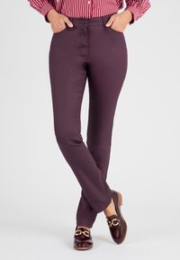 Pantalones burdeos de algodón elástico, con un diseño ajustado, bolsillos frontales y una textura suave. Combinados con mocasines marrones brillantes.