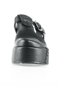 Chaussure à plateforme en cuir noir avec une semelle épaisse texturée et une bride argentée à boucle sur le dessus.