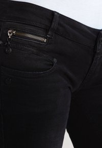 Svarta denimjeans med slim fit har en liten dragkedjeficka och en klassisk knappstängning. Tyget har en subtil textur och minimal blekning.