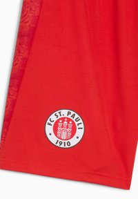 Röd sporttröja med en texturerad, andningsbar tyg. Inkluderar en cirkulär FC St. Pauli-logotyp med fästningsdesign, grundad 1910.