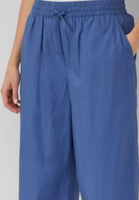 Pantaloni blu leggeri e comodi, con vita elasticizzata, cordino e tasche laterali. Texture liscia, design semplice senza motivi.