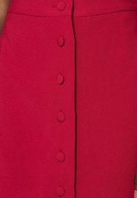 Punainen hame, jossa on teksturoitu kangas, etuosassa pyöreät nappikiinnitykset, sileä pinta ja istuva muoto.