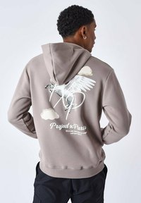 Sweat-shirt à capuche en coton beige clair, présentant un graphisme d'un cheval ailé et du texte au dos. Texture lisse et poignets côtelés.