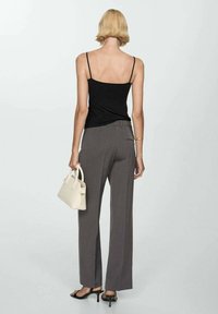 Schwarzes Trägertop, graue weit geschnittene Hose und eine kleine cremefarbene Handtasche; elegantes Design mit dünnen Trägern und glatter Textur.