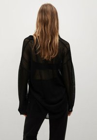 Schwarzes, übergroßes Strickshirt mit einem Netzdesign, langen Ärmeln und einem leicht gebogenen Saum. Der Stoff ist leicht und transparent.