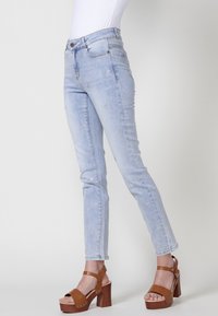 Jeans de mezclilla azul claro con un corte slim, que presentan detalles florales bordados y una cintura de altura media. Combinados con sandalias de plataforma color marrón.