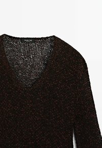 Svetr pletený s výstřihem do V, krátkými rukávy a volnou strukturou v tmavě hnědé barvě s světlejšími skvrnami. Štítek uvádí "Massimo Dutti."