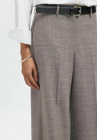 Graue Leinenhosen mit einem strukturierten Muster, Falten und seitlichen Taschen, kombiniert mit einem schwarzen Ledergürtel und einem silbernen Armband.