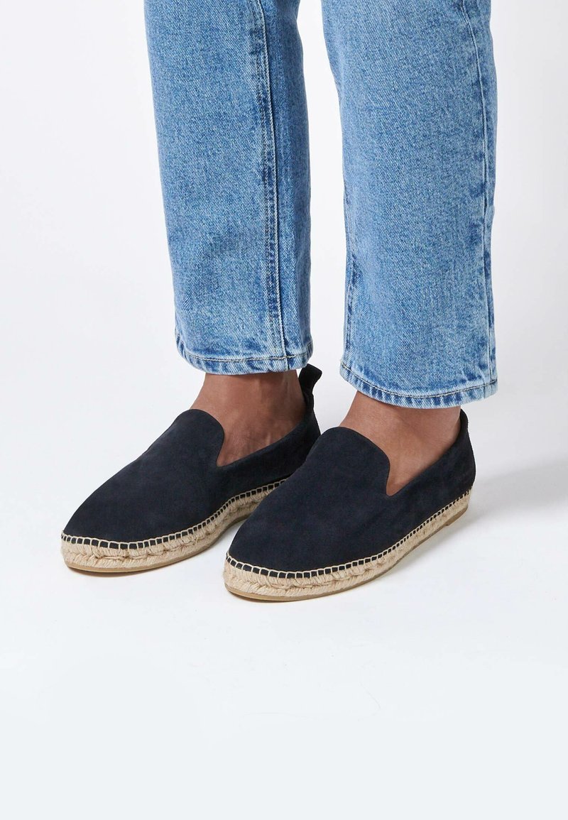Espadrilles en daim bleu marine avec un design à enfiler, semelle en jute et couture prononcée le long du bord, associées à un jean court bleu clair.