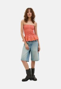 Narančasta navučena brezramna bluzica s peplum robom, v kombinaciji s svetlo modrimi denim bermudami in črnimi gležnjarji.