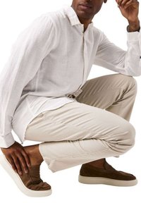 Witte linnen blouse met lange mouwen, beige broek en bruine instap sneakers met een gestructureerde bovenkant en een witte rubberen zool.