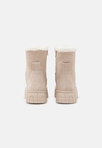 Stivali in suede beige da caviglia con una morbida fodera in pelliccia sintetica, dotati di cerniera laterale, suola in gomma testurizzata e dettagli rinforzati sul tallone.