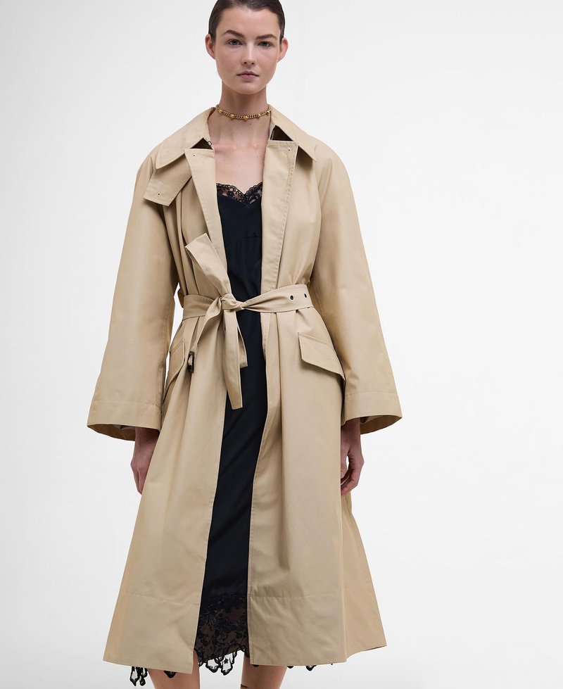 Beiger Trenchcoat mit einem taillierten Gürtel, großem Kragen und mattem Glanz. Verfügt über weite Ärmel und seitliche Taschen, getragen über einem schwarzen Spitzenkleid.
