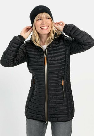 Zwarte pufferjack met een horizontaal doorgestikt patroon, zilveren rits en twee met rits afsluitbare zakken. Gecombineerd met een zwarte beanie.