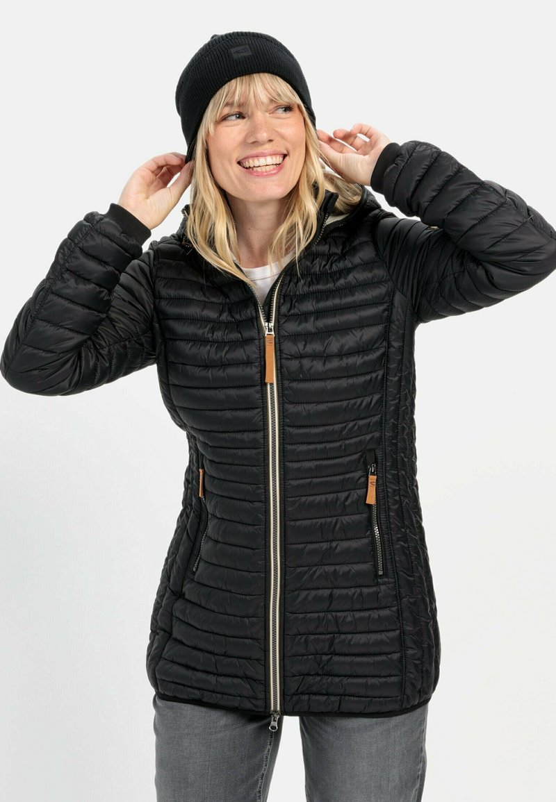 Zwarte pufferjack met een horizontaal doorgestikt patroon, zilveren rits en twee met rits afsluitbare zakken. Gecombineerd met een zwarte beanie.