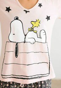 Lichtroze katoenen T-shirt met een zwart omlijnd grafisch ontwerp van Snoopy met Woodstock, verfraaid met zwarte sterren. V-hals ontwerp.