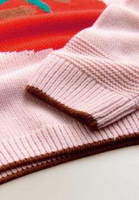 Pulover tricotat cu țesătură roz cu model în relief, margine maro și un design vibrant roșu cu accente verzi. Textură moale și pliuri suprapuse.