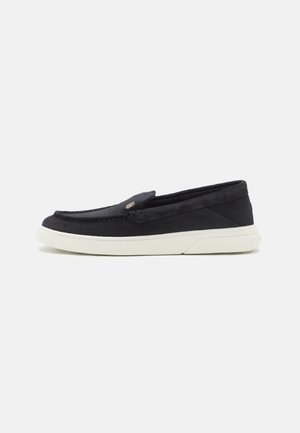 Marineblauwe instappers met een zachte suede buitenkant, voorzien van stikdetails en een witte rubberen zool. Minimalistisch ontwerp zonder zichtbare hardware.