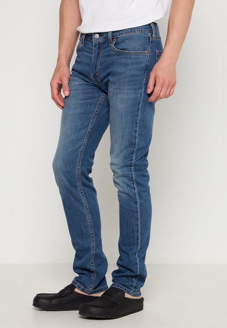 Slim fit niebieskie dżinsy z pięcioma kieszeniami, detalami szycia i wyblakłym wykończeniem, w połączeniu z czarnymi butami wsuwanymi.