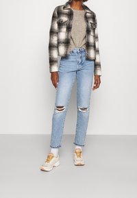 Giacca di flanella a quadri bianco e nero sopra un maglione grigio, abbinata a jeans azzurri strappati e sneakers chunky con dettagli rosa.